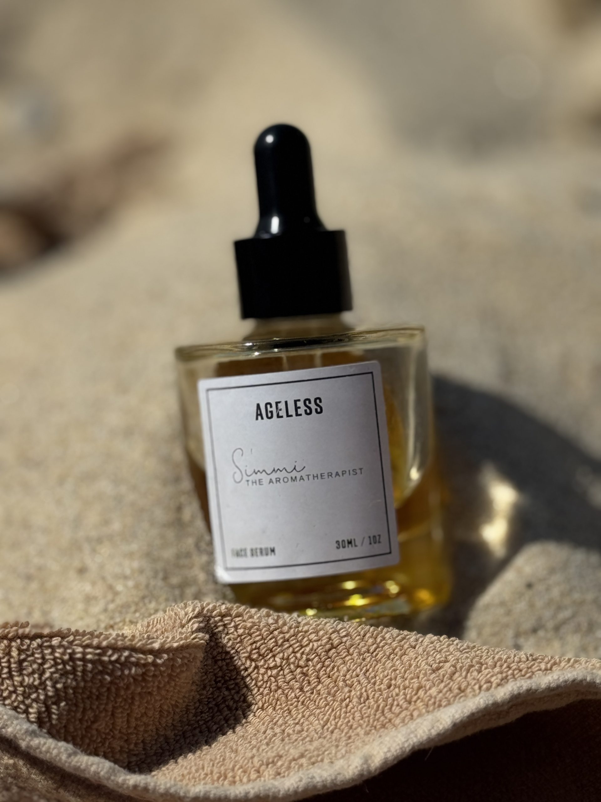 AGELESS Botanical Ritual Face Serum in a glass dropper bottle resting on soft linen in warm natural light.